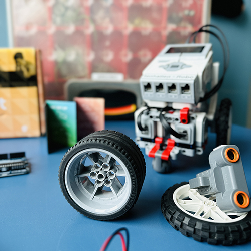 Delar från roboten Lego Mindstorms samt andra programmeringsdetaljer uppställda på ett bord. Foto. 